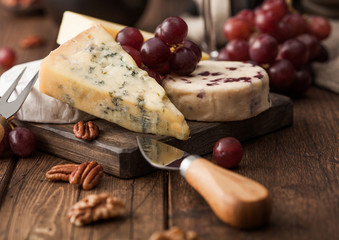 Selection of various cheese on the board and grapes on wooden background. Blue Stilton, Red Leicester and Brie Cheese and nuts.