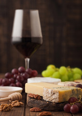 Glass of red wine with selection of various cheese on the board and grapes on wooden background. Blue Stilton, Red Leicester and Brie Cheese and bowl of nuts and honey.