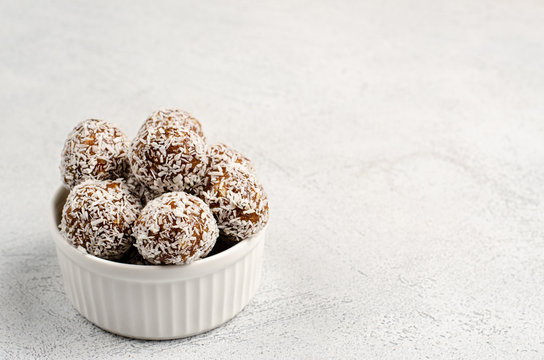 Energy balls of dates, nuts, oats, sprinkled with coconut powder closeup in a white plate on a white background background with copy space with place for your text. Healthy food. Raw dessert.