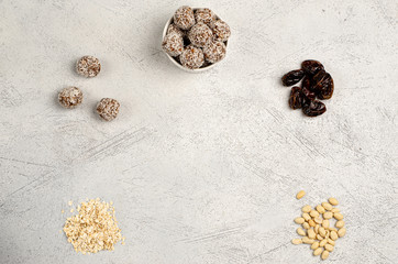 Fototapeta na wymiar Energy balls in a white plate and ingredients dates, oats, peanuts for their preparation on a gray background, flat lay, copy space. Healthy food. Raw dessert. View from above.