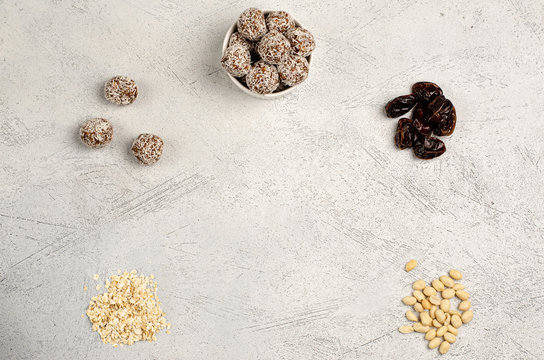Energy balls in a white plate and ingredients dates, oats, peanuts for their preparation on a gray background, flat lay, copy space. Healthy food. Raw dessert. View from above.