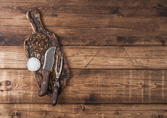 Vintage fork and knife for meat on wooden chopping board with salt and pepper on wooden table background. Space for text