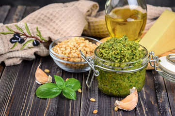 Pesto sauce in a jar with pine nuts, parmesan and garlic over dark wooden background