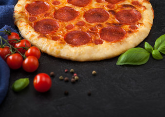Fresh round baked Pepperoni italian pizza with tomatoes with basil on black background with blue linen towel.