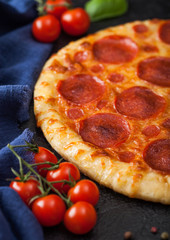 Fresh round baked Pepperoni italian pizza with tomatoes with basil on black background. Top view