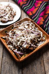 Mexican chilaquiles with mole sauce and fresh cheese on wooden background