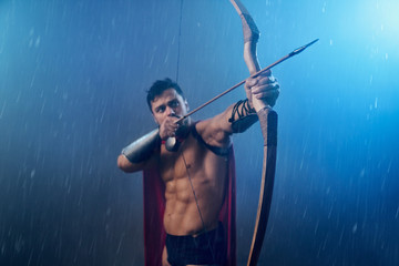 Muscular mature spartan shooting from bow.
