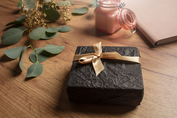 Beautiful gift on a wooden table with flowers, a notepad and a candle. Gift box. Holiday surprise. Lifestyle. View from above. 