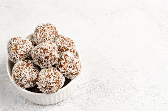 Energy balls of dates, nuts, oats, sprinkled with coconut powder closeup in a white plate on a white background background with copy space with place for text. Healthy food. Raw dessert.