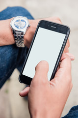 Mockup image of mans hands holding an empty smart phone, mobile phone with blank screen on thigh sat on a bench in natural light. perfect for copy of composite phone messages.