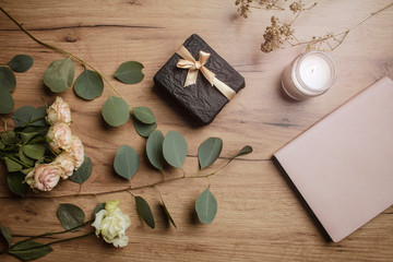 Beautiful gift on a wooden table with flowers, a notepad and a candle. Gift box. Holiday surprise. Lifestyle. View from above. 
