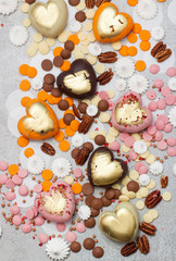 Fototapeta na wymiar Assorted pink, orange, brown and green chocolate hearts with meringues, pecan nuts and chocolate drops on grey background