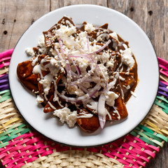Mexican chilaquiles with mole sauce and fresh cheese on wooden background