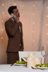 selective focus of elegant man talking on smartphone while standing near served table in restaurant