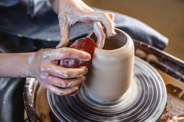 Potter working on a Potter's wheel making a vase. Woman forming the clay with her hands creating jug in a workshop