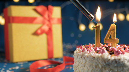 White birthday cake number 14 golden candles burning by lighter, blue background with lights and...