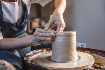 Potter working on a Potter's wheel making a vase. Woman forming the clay with hands creating jug in a workshop. Close up
