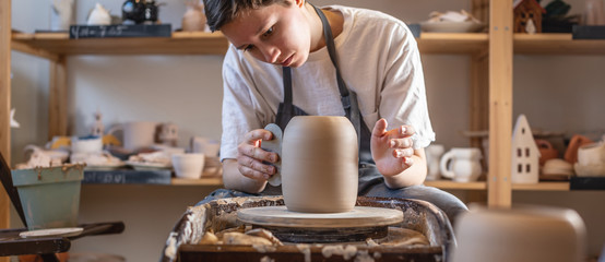 Potter working on a Potter's wheel making a vase. Master processing the formed jug giving it the...