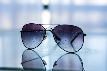 Gafas de sol con gotas de lluvia en los cristales, en primer plano sobre una mesa de cristal con...