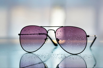 Primer plano de gafas de sol con gotas de lluvia en los cristales, reflejos y fondo desenfocado. 