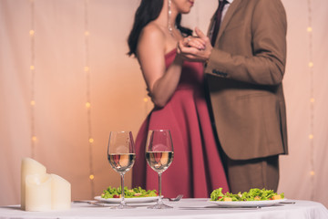 cropped view of elegant man and woman dancing in restaurant near served table