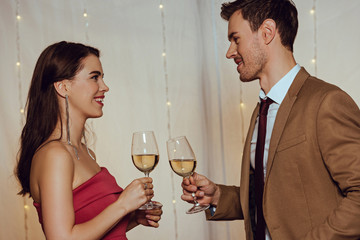 side view of happy, elegant couple looking at each other while holding glasses of white wine