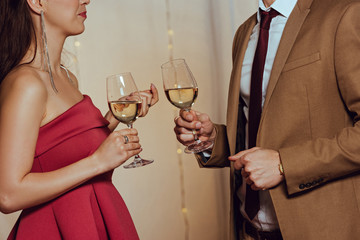 cropped view of elegant man and woman holding glasses of white wine in restaurant