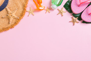 Beach accessories with straw hat, sunscreen bottle and seastar on pink background top view with copy space