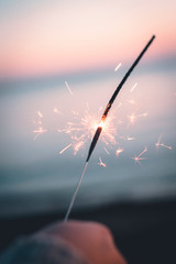 A hand holding a sparkler in the beach