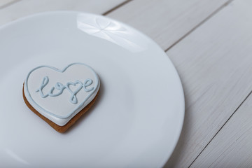 Heart shape gingerbread cookie on white plate standing on white wooden table background. 14 February Valentine's day and love concept. Place for text.