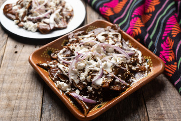 Mexican chilaquiles with mole sauce and fresh cheese on wooden background