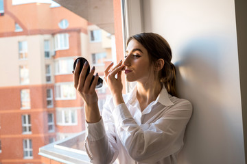 girl doing itself makeup near window in the background before taking a photossesion.