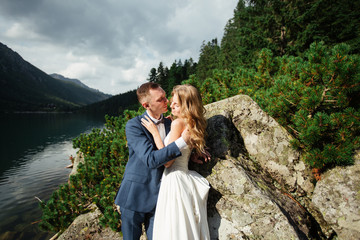 Naklejka premium Sensual wedding couple standing on the stony shore of the Sea Eye lake in Poland.