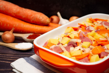 Sliced ​​meat, onions, carrots and potatoes in an orange baking dish. Close-up of meat goulash with vegetables in orange baking dish