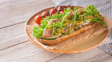 Food banner: bruschetta with raw smoked meat, cream cheese, pea micro-greens and pesto sauce, cherry tomatoes on a round ceramic plate