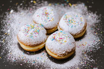 Donuts in powdered sugar and colored sprinkles on a black background. 