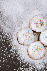 Donuts in powdered sugar and colored sprinkles on a black background. 