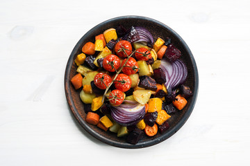 Diet baked vegetables. Beets, carrots, pumpkin, red onions, cherry tomatoes and potatoes on a brown clay plate