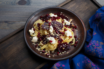 Pasta with slices of beets, soft blue cheese, pomegranate seeds and nuts on a brown plate on a dark wooden background. Italian fusion cuisine