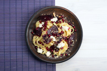Pasta with slices of beets, soft blue cheese, pomegranate seeds and nuts on a brown plate....