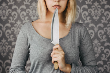 woman blonde holding a kitchen knife in her hand, threat, murder, domestic violence - obrazy, fototapety, plakaty