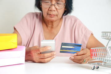 An elderly Asian woman holding a simulated credit card is not the real thing. Shopping online. Senior community concept
