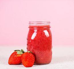 Red berry smoothie in a glass jar on a pink background. Selective focus.