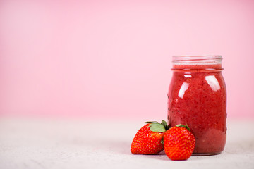 Red berry smoothie in a glass jar on a pink background. Selective focus.