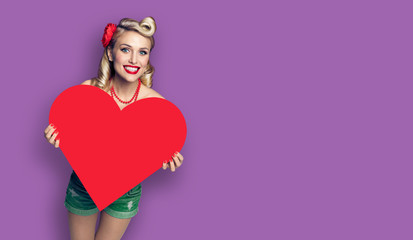 Woman holding red paper heart shape. Pin up girl. Retro fashion and vintage concept picture. Violet purpure color background. Copy space for some slogan or sign text. Valentine or Like symbol.