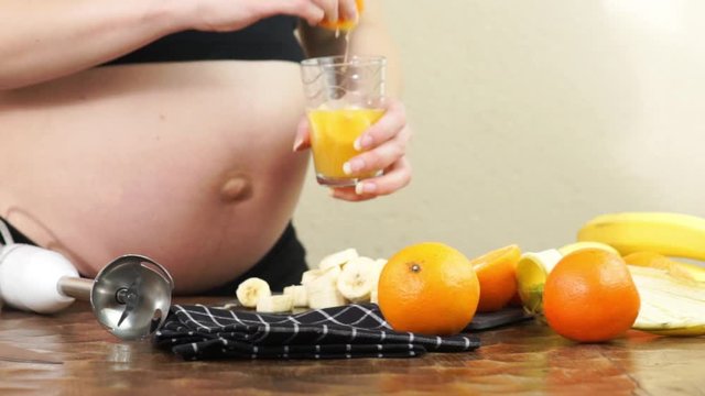 Third trimester pregnant woman prepares some freshly squeezed orange juice to make a healthy fruit smoothie with blender