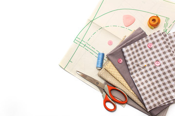 Tools for sewing on a white background. A set of fabrics, a pattern, threads, buttons, scissors. Flat lay, copy space.