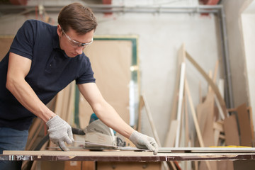 Male carpenter in glasses measures board with centimeter tape in workshop