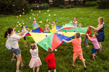 Happy kids waving rainbow parachute full of balls - 322617790