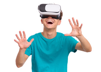 Happy teen boy wearing virtual reality goggles watching movies or playing video games. Cheerful smiling teenager looking in VR glasses. Funny child experiencing 3D gadget technology. - 322618323